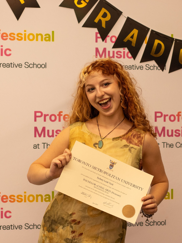 A Professional Music student holding up their certificate and smiling at the camera. 